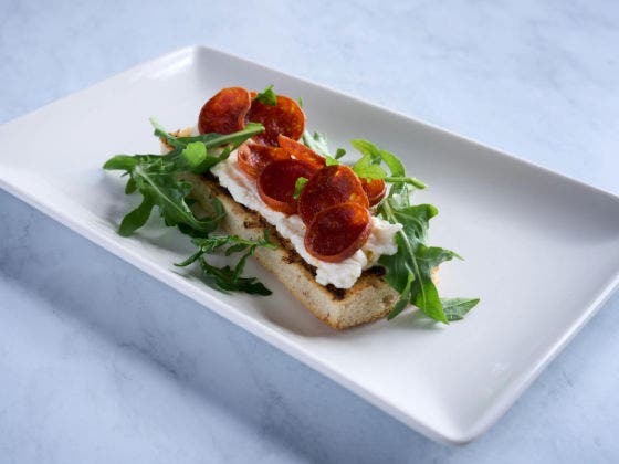 plated focaccia bread, topped with ricotta, pepperoni and greens