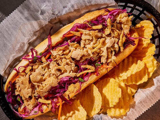 Chicken slices on a hoagie bread with purple cabbage and crinkle chips on the side