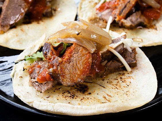 Smoked beef chuck shoulder roast covered in barbacoa sauce on a slightly toasted corn tortilla with onions and cilantro on a black plate