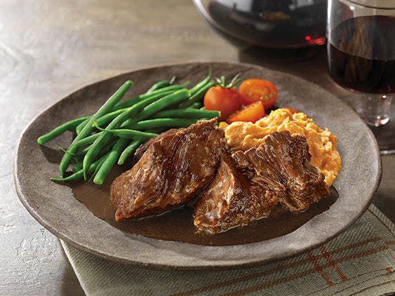 Chuck shoulder roast on a plate with gravy, green beans, mashed sweet potatoes and tomatoes.