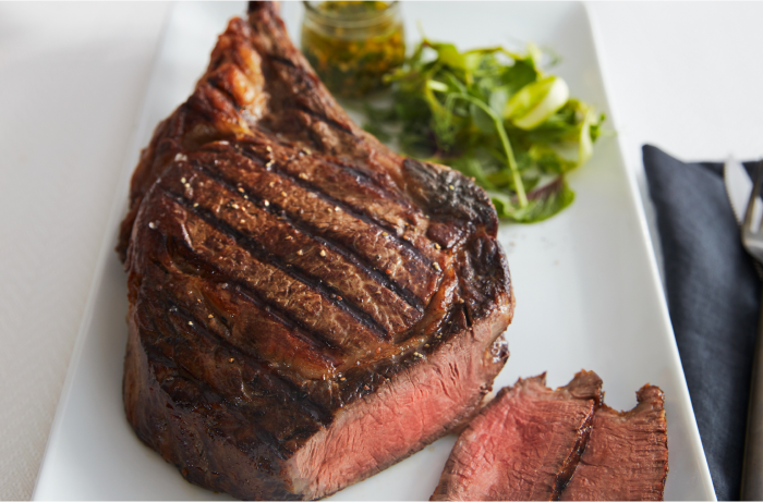 Tomahawk Cut Steak With Side of Greens on a White Retangular Plate