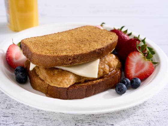 French toast chicken sandwich with cheese and a side of strawberries and blueberries 