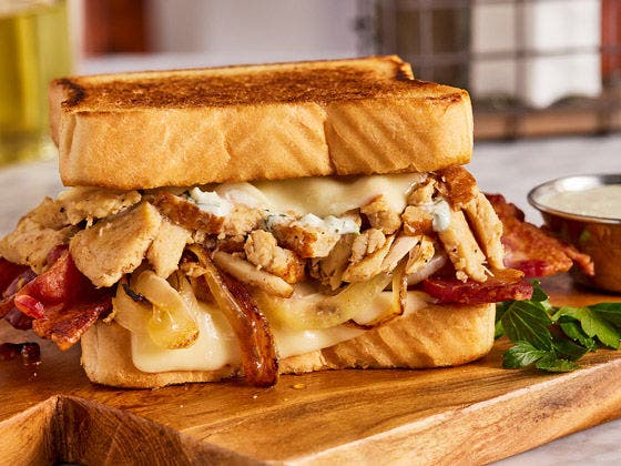 Wooden plated chicken sandwich with chicken, bacon, cheese, grilled onions, and jalapeno ranch on texas toast