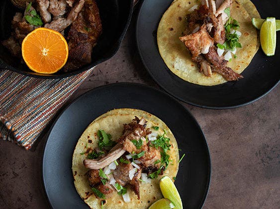 Sous vide pork carnitas on a tortilla with onions, cilantro and lime on a black plate