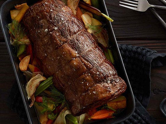 Braised chuck roast on a pan with onions, carrots and celery, next to a plate of pickled shallots and roasted beets.