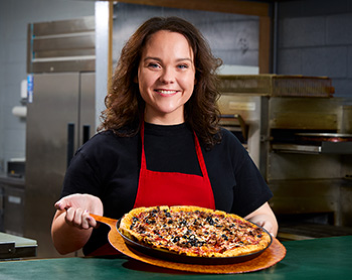 Girl with red apron holding a pizza on a wooden sleet