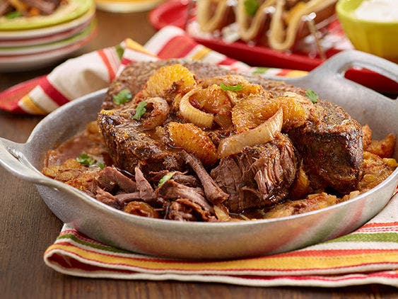 A bowl with braised beef in sauce, topped with oranges and onions.