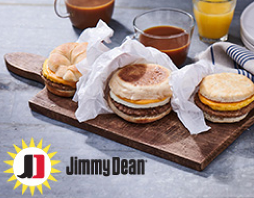 Three sausage breakfast sandwiches on a wooden board and drinks on the side