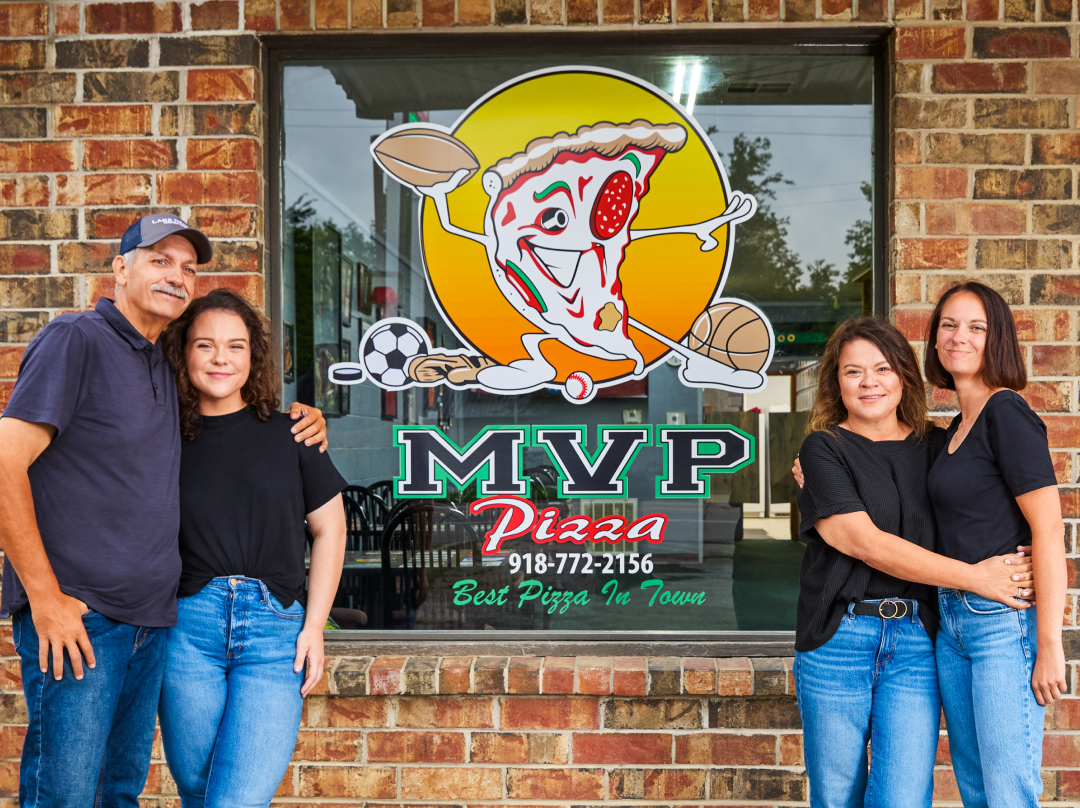MVP Pizza window logo with the owners and employees taking a picture in front of it