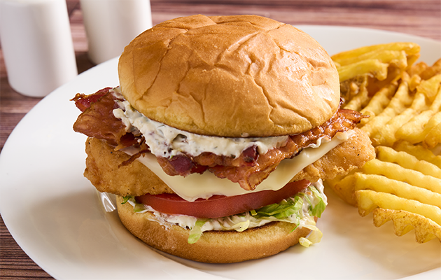 Image of crispy chicken bacon swicy pickle ranch sandwich with a side of fries.