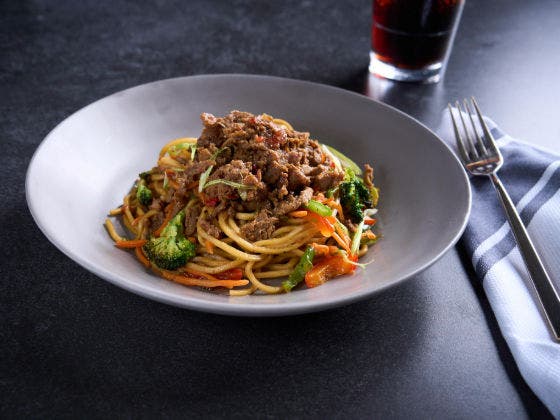 Plated noodles topped with beef, bell peppers and broccoli florets  