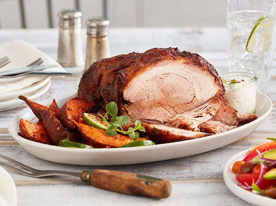 Roasted pork butt sliced with vegetables and garnish served on a white plate placed on a table.