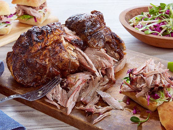 Smoked pork shoulder on a cutting board, with a bun and some pulled pork.